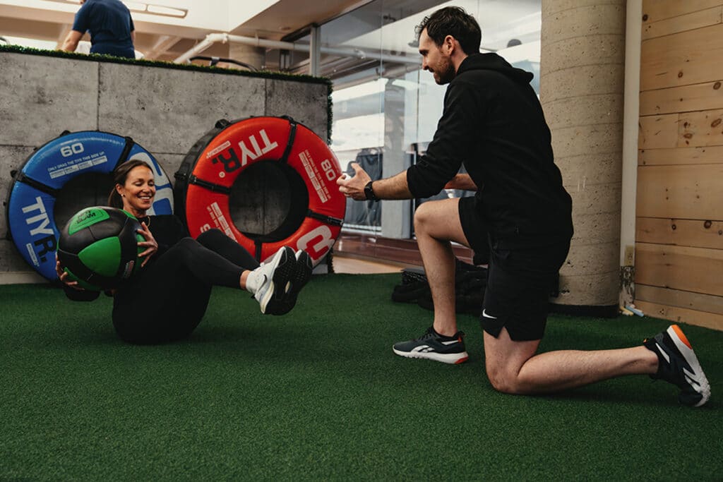 Personal trainer instructs woman as she works out using medicine ball on turf