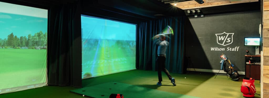 man hits golf ball inside PGA golf simulator.