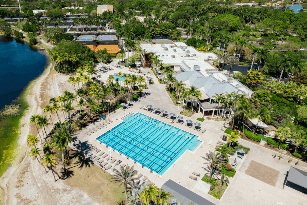 Aerial view of Midtown Weston featuring a lap pool, lounge chairs, tennis courts, and lush tropical landscaping, showcasing the club’s premium outdoor amenities in South Florida.