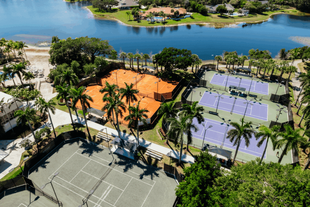 Aerial view of Midtown Athletic Club Weston’s tennis complex, showcasing clay and hard courts surrounded by palm trees and water — a premier tennis destination in Weston, FL for competitive and recreational play.