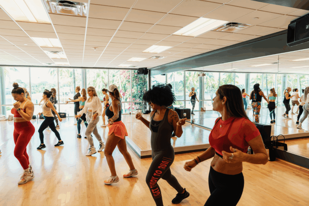 Group fitness class in a bright, spacious studio at Midtown Weston, featuring natural light, mirrored walls, and energetic participants engaged in a dance-based workout.