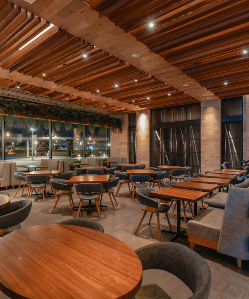 chi chromium arc Interior of a contemporary restaurant with a warm, inviting atmosphere. The space features neatly arranged wooden tables and cushioned chairs, a ceiling with wooden slats and recessed lighting, and large windows that let in ample natural light. Greenery is suspended above the windows, adding a touch of nature to the modern design.