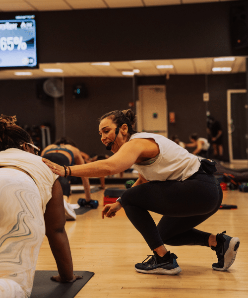 Group fitness instructor coaches woman who is in plank position